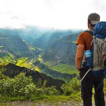 man with a backpack looking out over mountains and green pastures