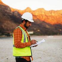 man wearing white hard hat and yellow reflective vest looking at paperwork