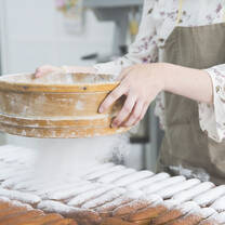 A woman dusting freshly made pastries with powdered sugar