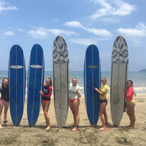 students holding up surfboards on the beach