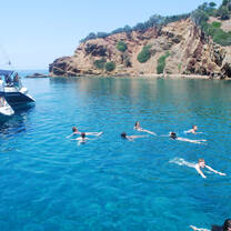students swimming off back of sailboat in turquoise water