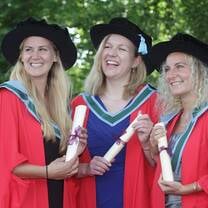 NUI Galway masters students graduating with cap, gown, and diplomas