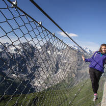 girl walking across high bridge with mountains in the background