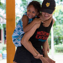 A volunteer carrying a young girl on her back while smiling