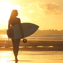women walking on beach with surfboard at sunset