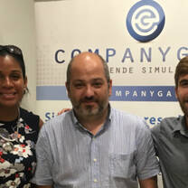 three people smiling in front of wall with company logo on the wall