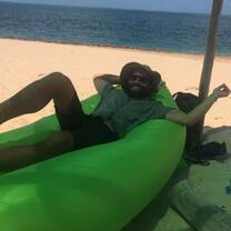 man laying down on a green inflatable chair on beach 