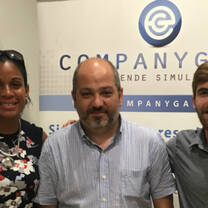 three people smiling in front of wall with company logo on the wall