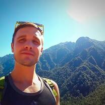 selfie of a man in front of large green mountain