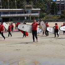 students wearing red shirts smiling with surf boards on the beach 