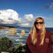 blonde haired girl in red sweatshirt smiling in front of Australian beach 