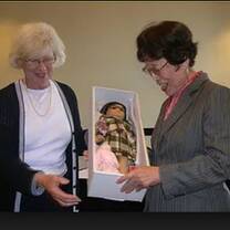 Two old ladies holding a doll in a box