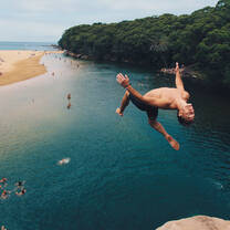 guy doing a backflip off a cliff into the water