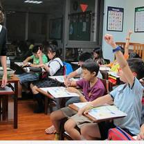 The girl write something on the board while the students raising their hands