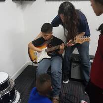 a little boy playing guitar while a man his teaching him