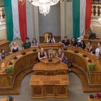 group of students sitting in a horseshoe shape in building with italian flags behind them