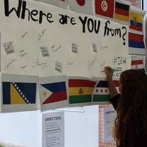 girl writing on a sign called where are you from with flags 