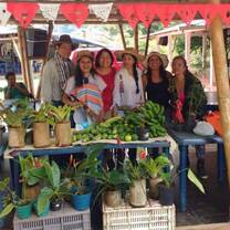 Group of people behind a market stand where fruit, vegetables and flowers are sold