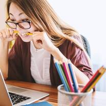 the girl is biting the pencil while looking at her laptop
