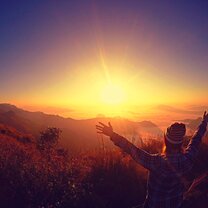 hiker with arms raised in front of sunset