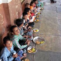 Children are eating food on metal plates provided by the organization