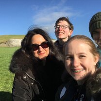 A field trip to Newgrange, featuring the reviewer, two classmates, and the instructor smiling with the ancient tomb in the background