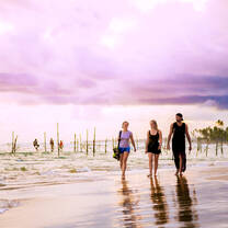 three girls walking down beach at sunset 