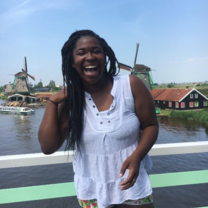 A young woman in a white blouse tosses her hair and laughs at the camera while she stands in front of windmills in Zaans Schans, Netherlands