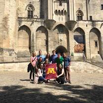 Students standing in front of a beautiful building holding the UofM flag. 