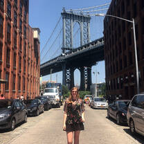 An intern stands beneath Brooklyn Bridge on a sunny day.