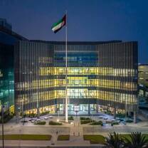 The flagpole stands tall with the UAE flag waving in front of Khalifa University's beautiful concrete and steel structure