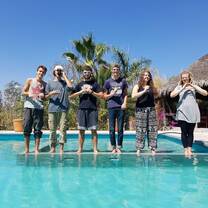 group of six people standing next to a pool in Mexico spelling Mexico with their fingers