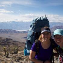 two girls smiling with packs on backs while backpacking in the desert