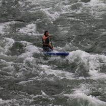 guy kneeling on stand up paddle board going through rapids