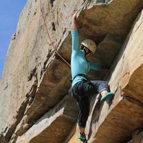 girl rock climbing reaching over ledge for a hold
