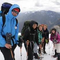 group of five people in backpacks and snowshoes traveling in mountains