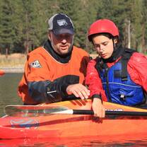 a student in a kayak learning to roll from an instructor 