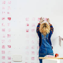 Student working on a piece of art, pink squares on a wall.