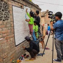 Video camera operator filming children writing on a wall