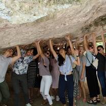 Group of students standing under a rock pretending to hold it up with shocked and strained expressions on their faces