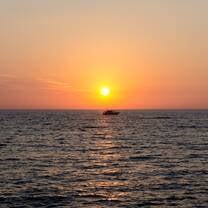 Sunrise over the coast of Ortigia with a boat crossing in front of the sun