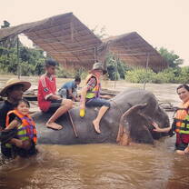 Young teachers riding an elephant walking through water