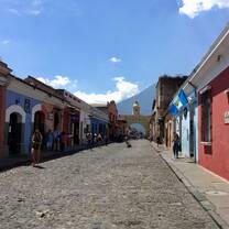 a long view down a street adorned with colorful buildings with a volcano in the distance