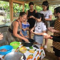 a woman with her hand in a cooking bowl shows a group of five students how to make Pupusas