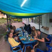 (group of people sitting around outdoor table, smiling with barbecue food)