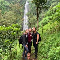 (three girls in lush green jungle, with big waterfall in the background)