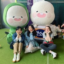 3 girls sitting on the ground in front of characters doing the korean flower pose