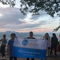 Three people holding a CISabroad flag posing against the sunset at Seoul Tower