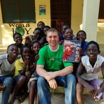 Male volunteer in Kenya smiles with a group of children.