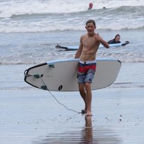 Teen boy gives thumbs up with surf board by waves